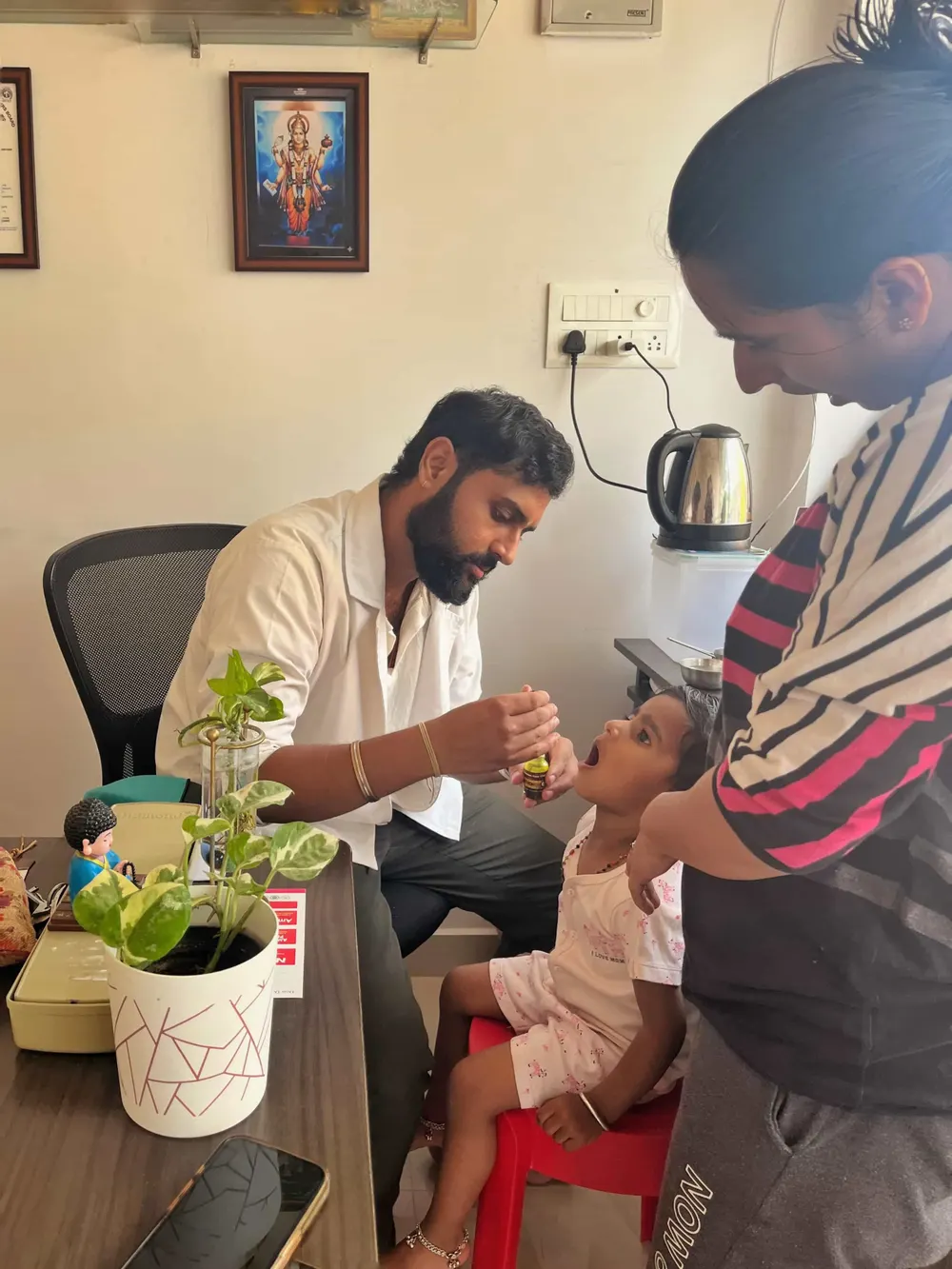 Dr. Rohit S. Patil giving Swarna Bindu Prashana drops to a young child while her mother watches